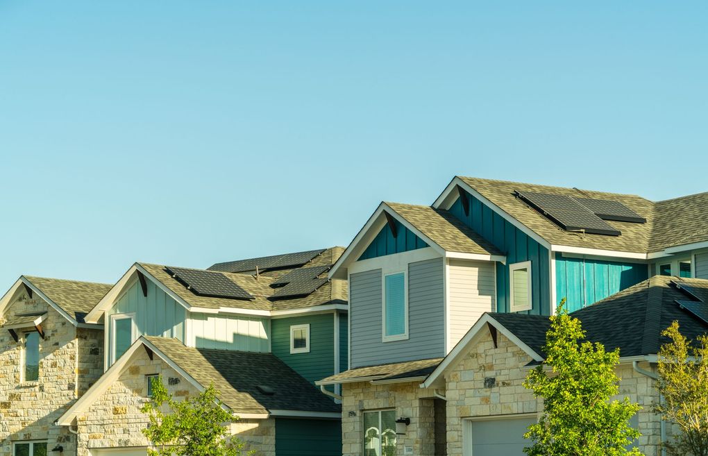 Row of colorful houses with solar panels on roofs against a clear blue sky.