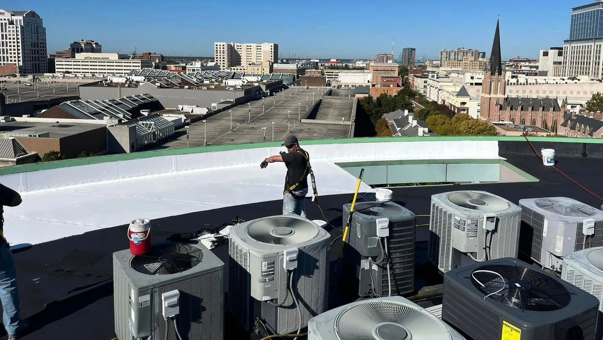 Workers on a rooftop with HVAC units; city skyline in background.