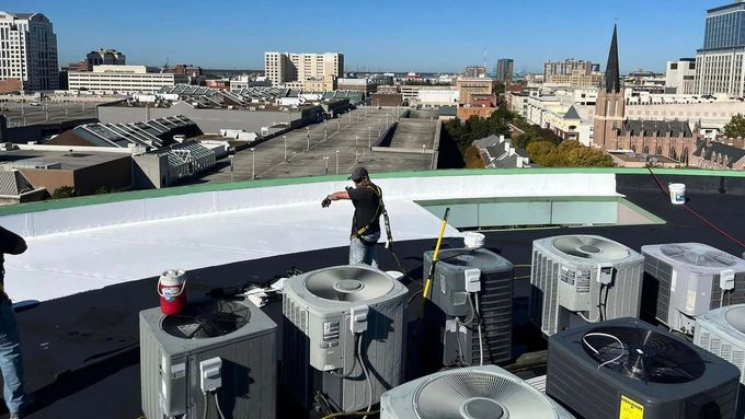 Workers on a rooftop with HVAC units; city skyline in background.
