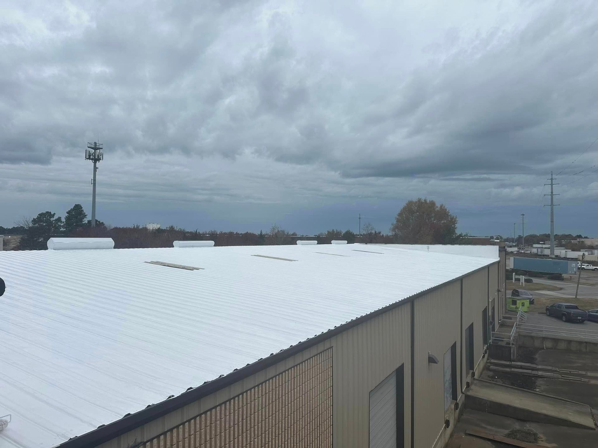 Building rooftop with metal sheeting under cloudy sky, cell tower in the distance.