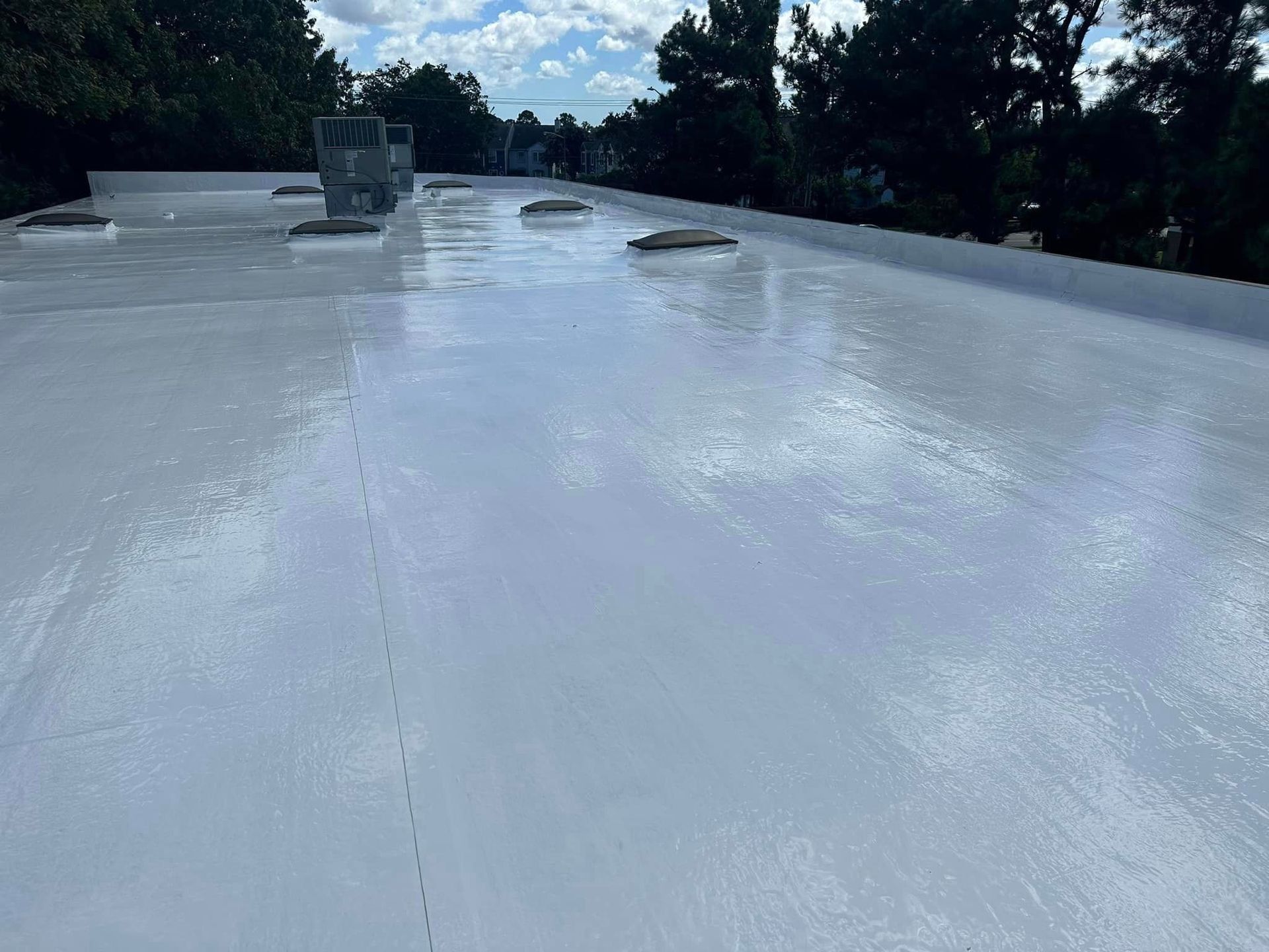 Flat, light gray commercial roof with vents under a partly cloudy sky.