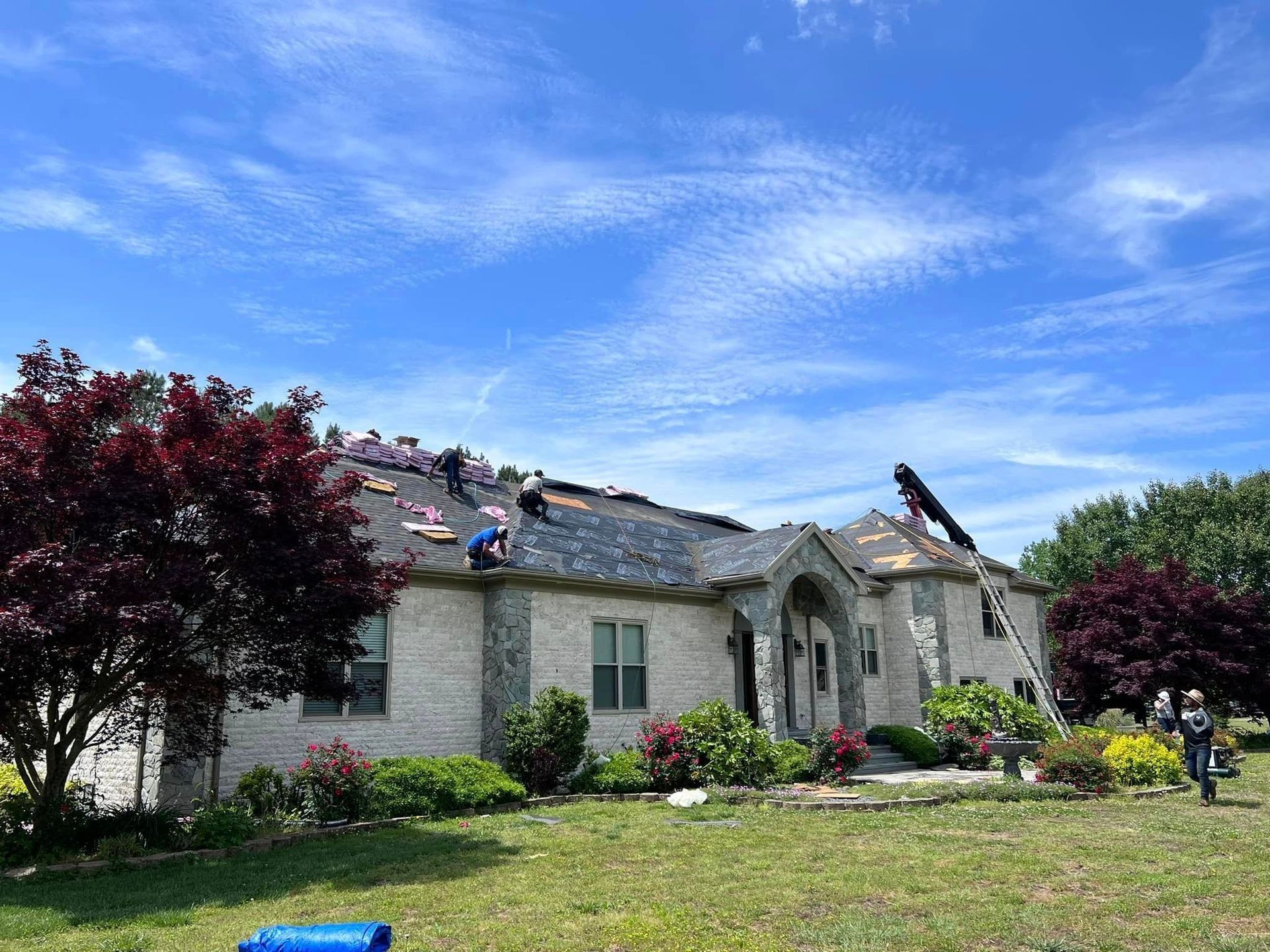 Workers installing a new roof on a two-story brick house on a sunny day.