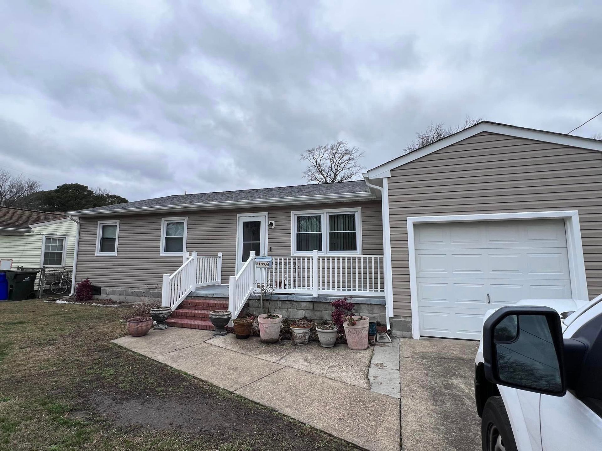 Ranch-style house with gray siding, attached garage, and small porch under a cloudy sky.