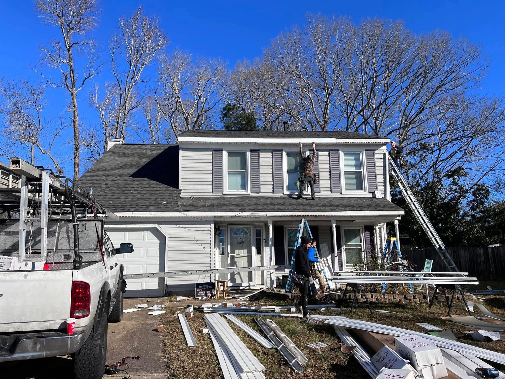 House exterior being renovated; workers on roof and ground, white truck, blue sky.