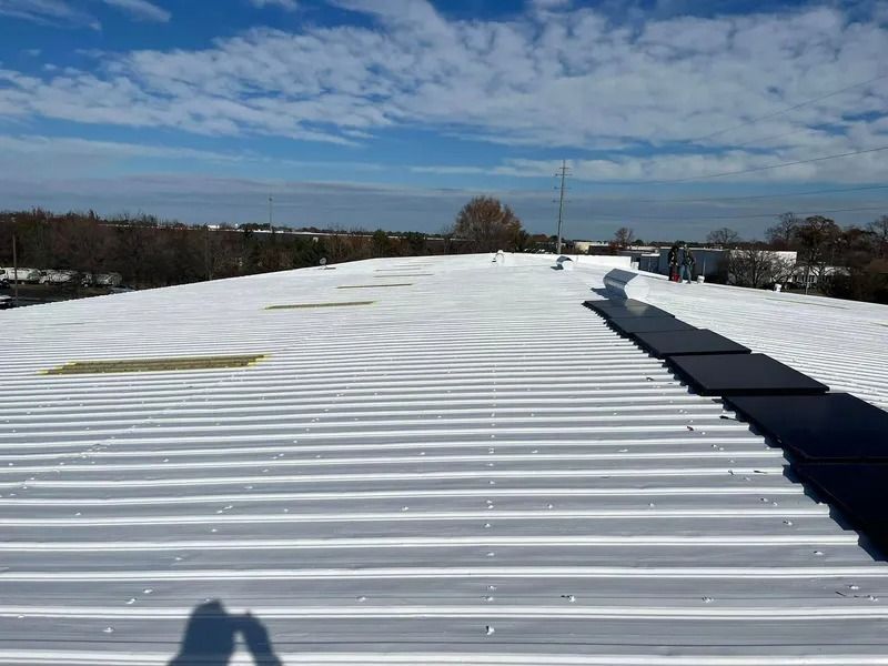 White, corrugated metal roof with solar panels. Blue sky with clouds.
