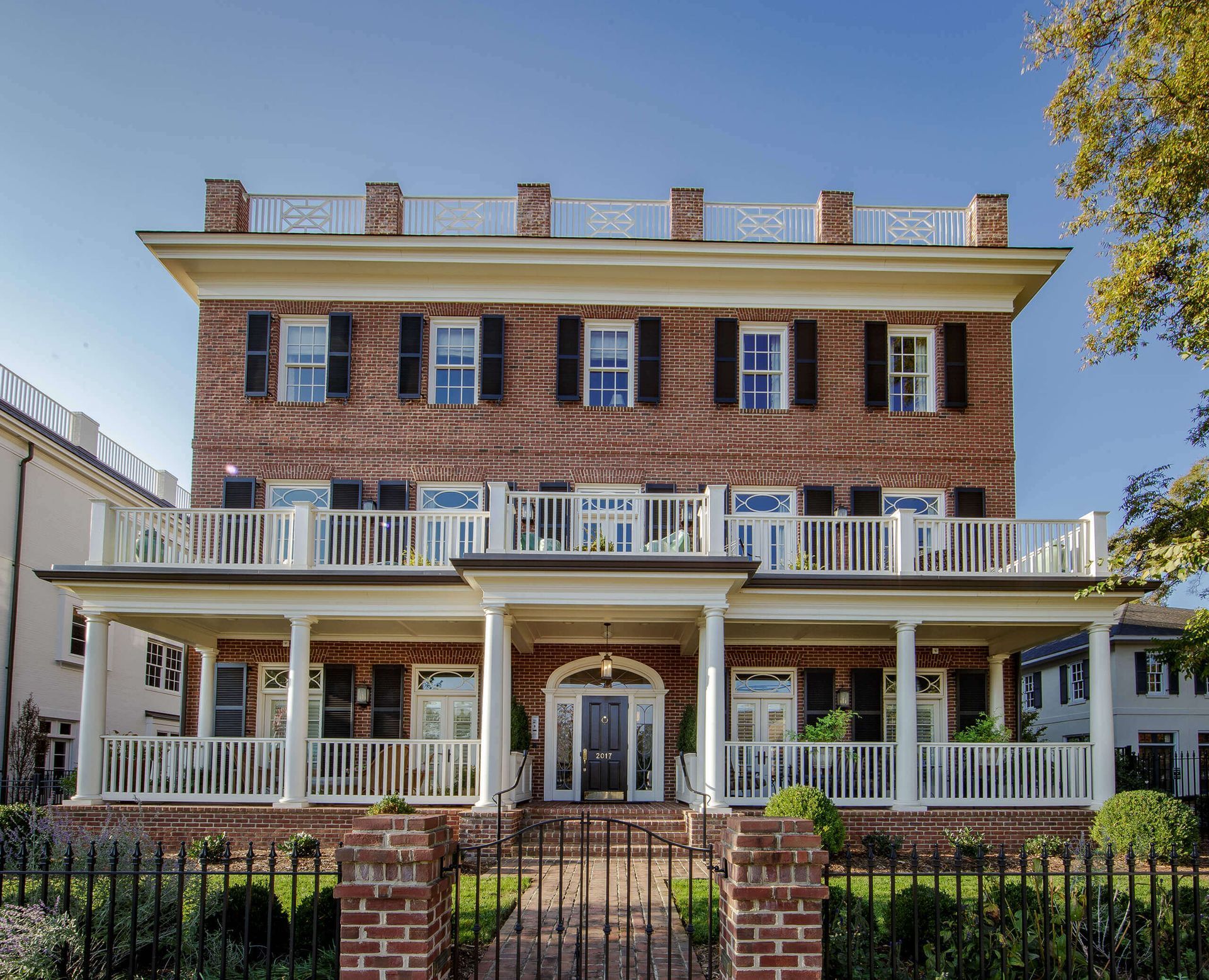 Three-story brick building with white balconies and trim, black shutters, and a wrought-iron fence.