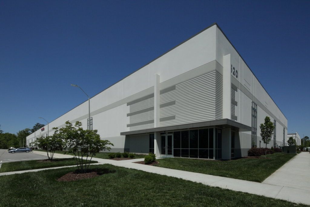 Large white industrial building with glass front, under a blue sky.