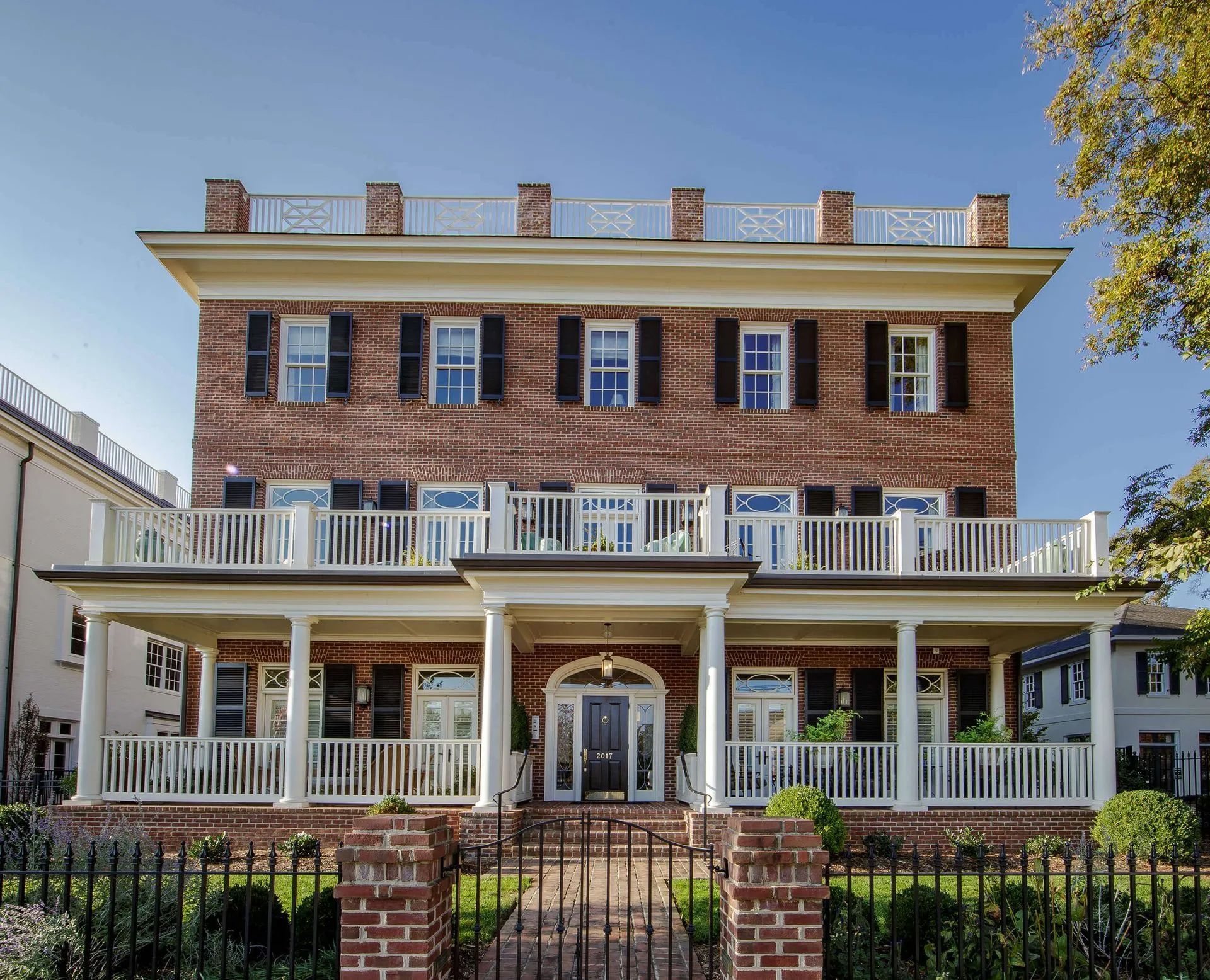 Three-story brick building with white balconies and trim, black shutters, and a wrought iron fence.