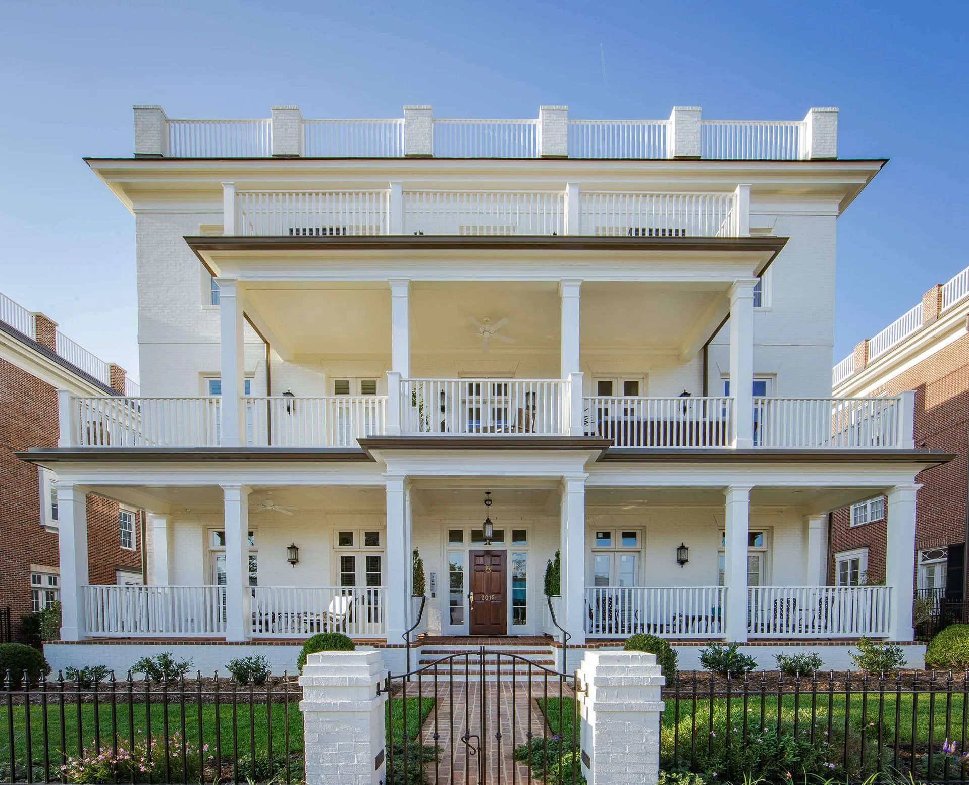 White three-story house with columns and balconies, a black gate, and brick walls on either side.