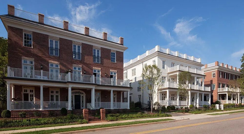 Row of three-story brick and white buildings with balconies under a blue sky.