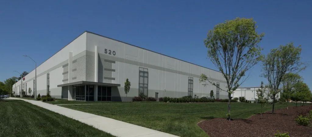 White industrial building with large windows, sidewalk, and trees under a clear blue sky