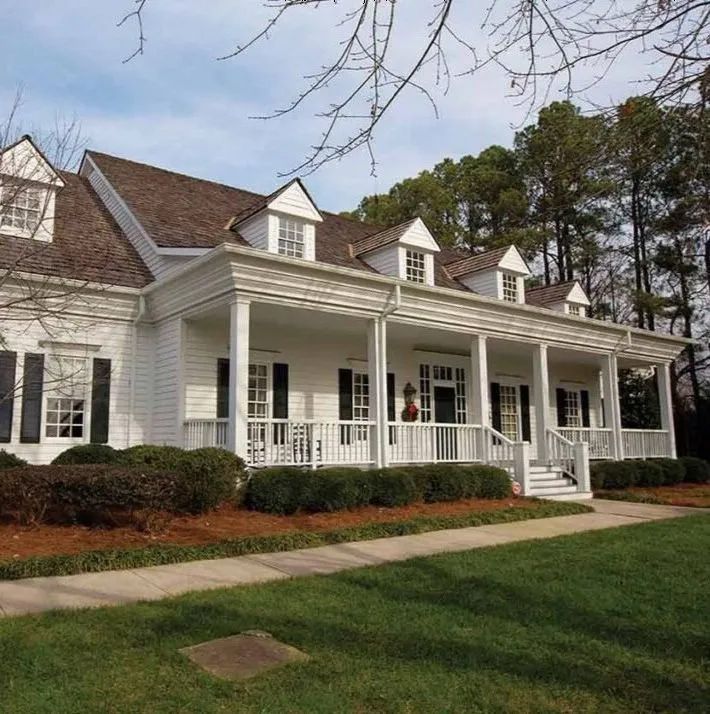 White house with porch, black shutters, brown roof, and green lawn.