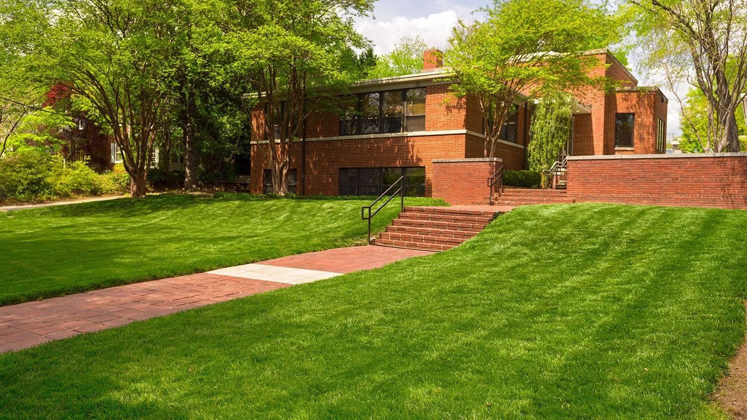 Brick building with a red walkway, steps, and a green lawn shaded by trees
