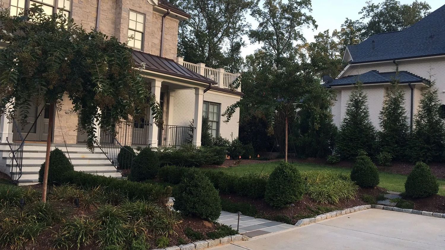 Upscale homes with manicured hedges and trees along a quiet residential driveway