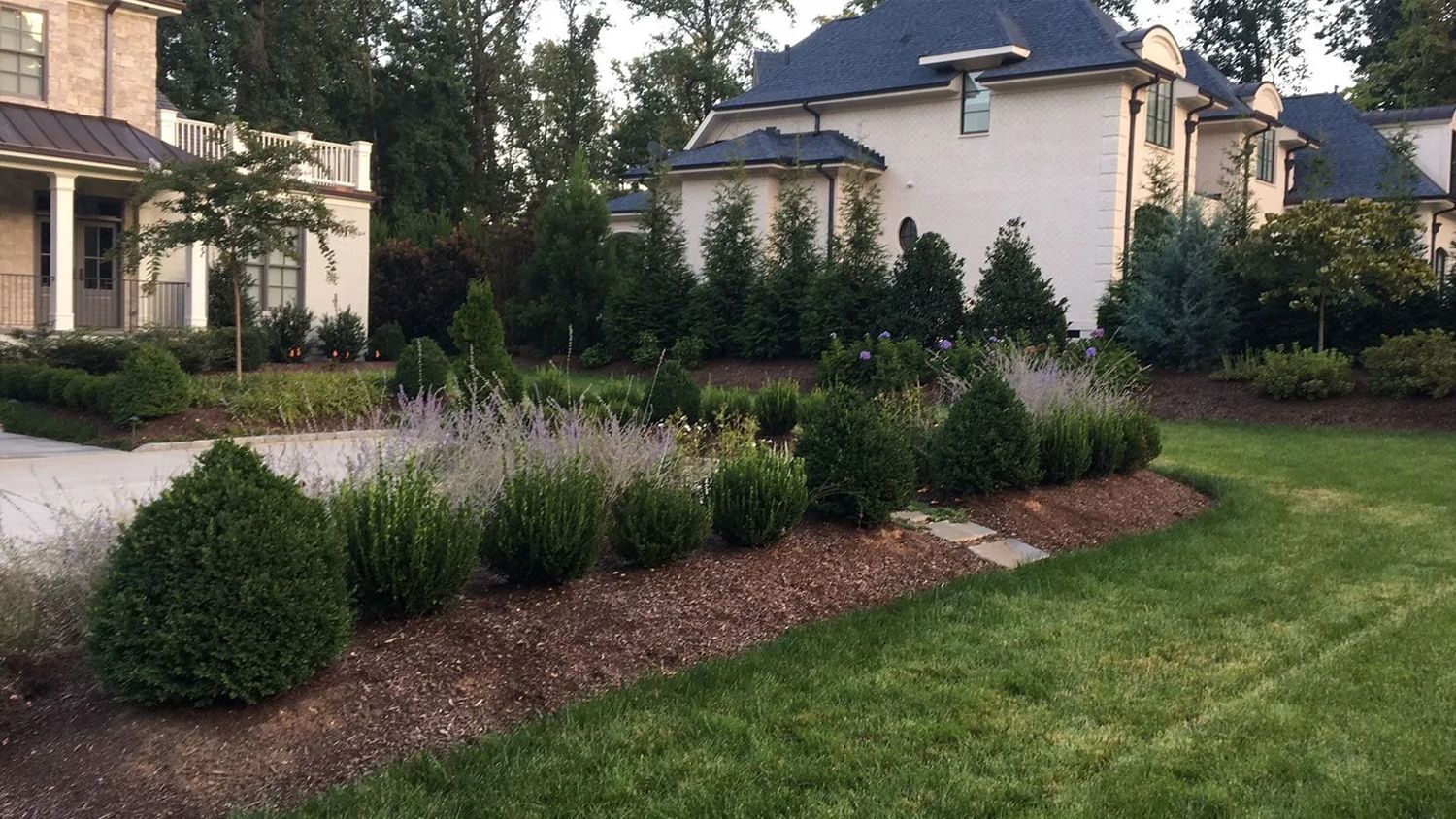 Landscaped front yard with shrubs, flowers, and mulch beside a house and green lawn