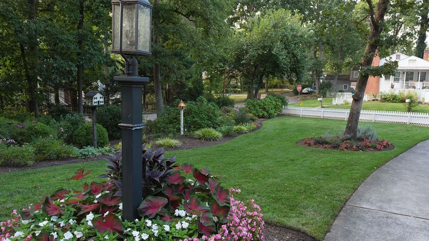 Landscaped garden path with a black lamp post, flowers, and trees beside a curving walkway.
