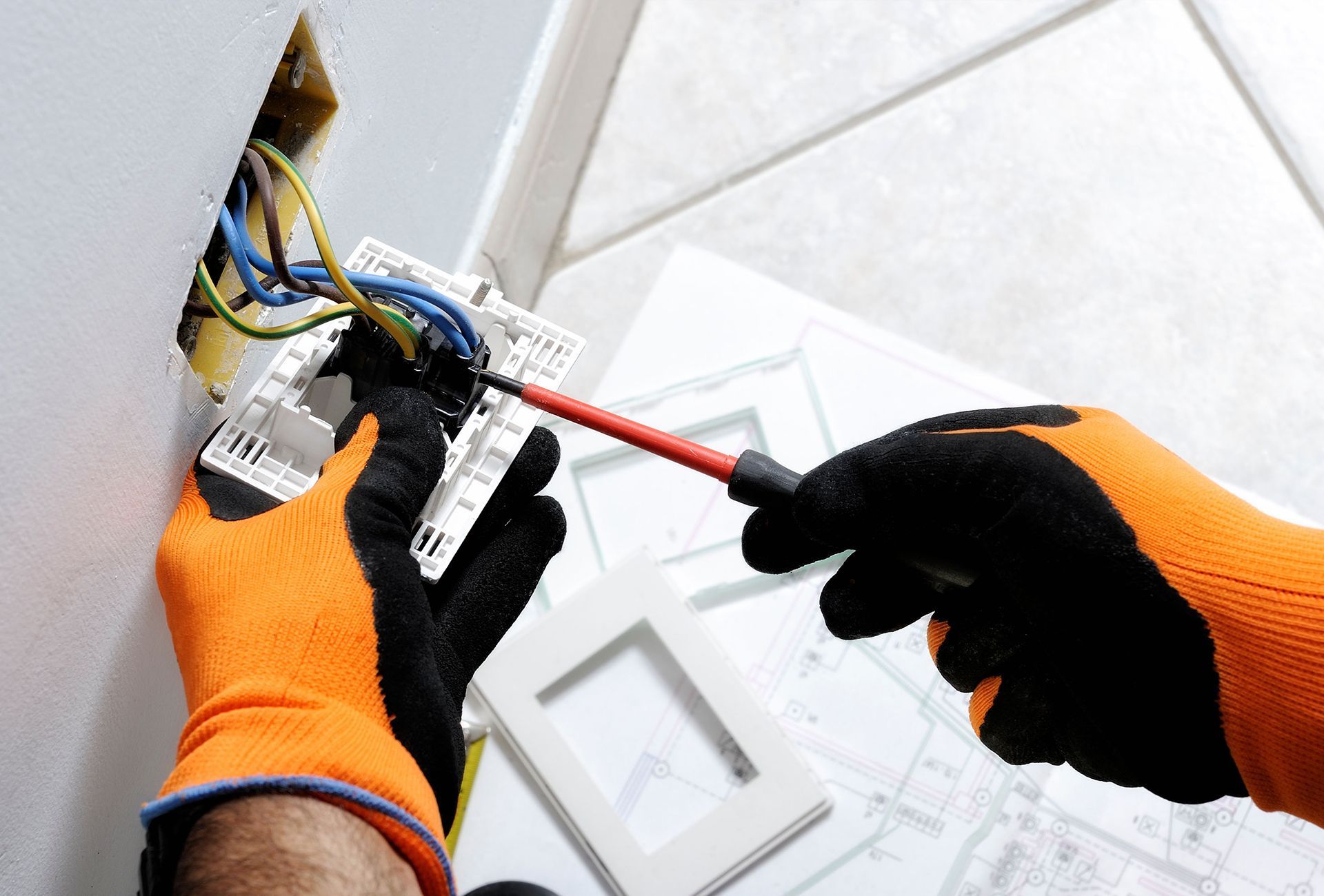 a person wearing orange and black gloves is working on an electrical outlet with a screwdriver