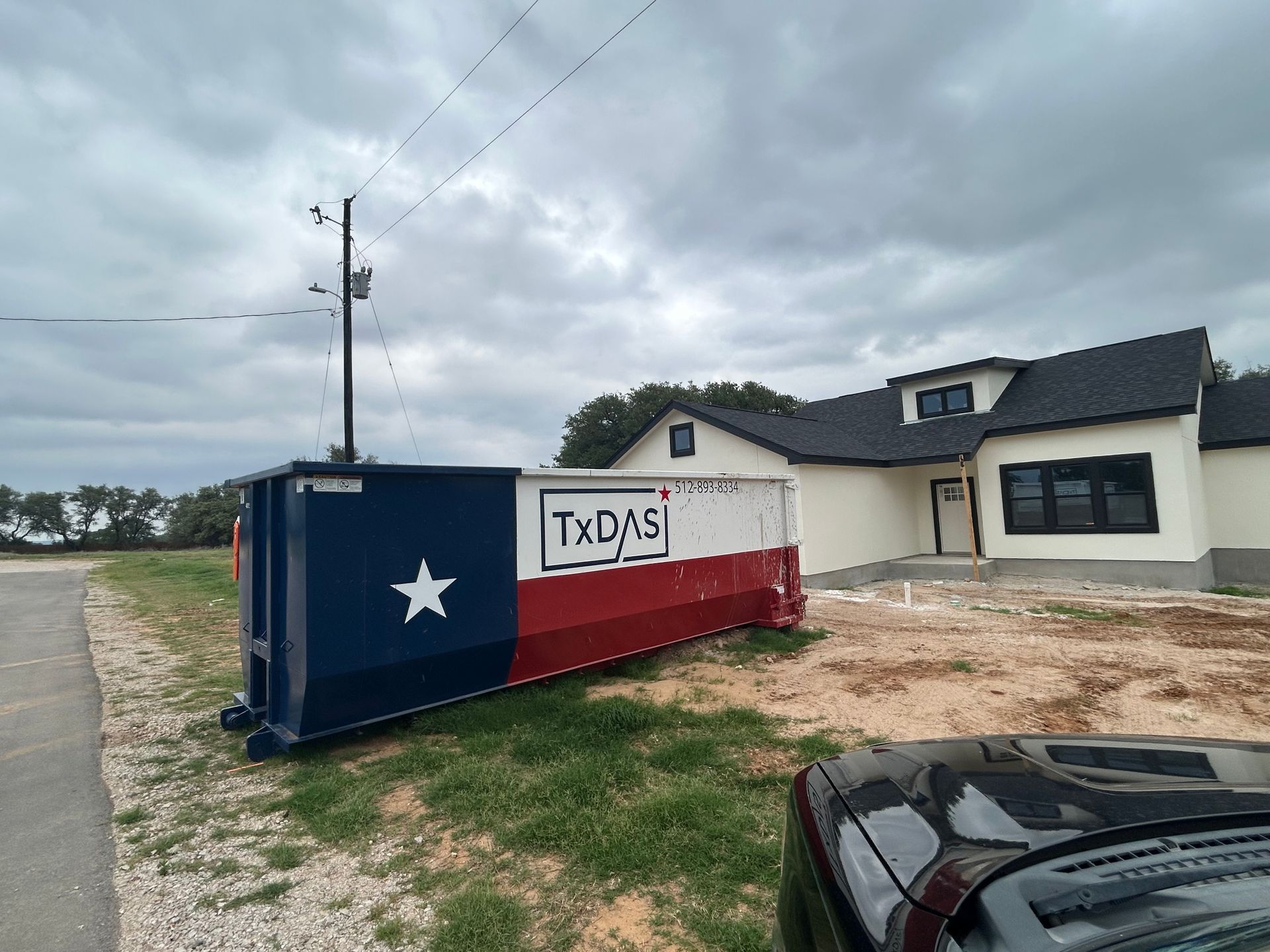 A dumpster painted with the Texas flag sits on a construction site next to a new house.