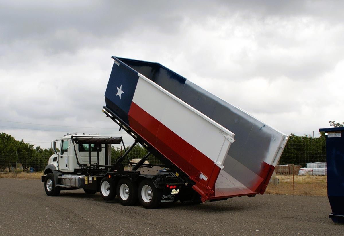 Dump truck with the Texas flag painted on the container, lifting up to dump a load.