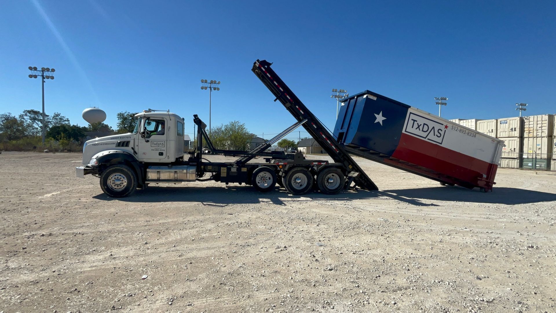 A truck lifts a container painted with the Texas flag in a dusty lot.