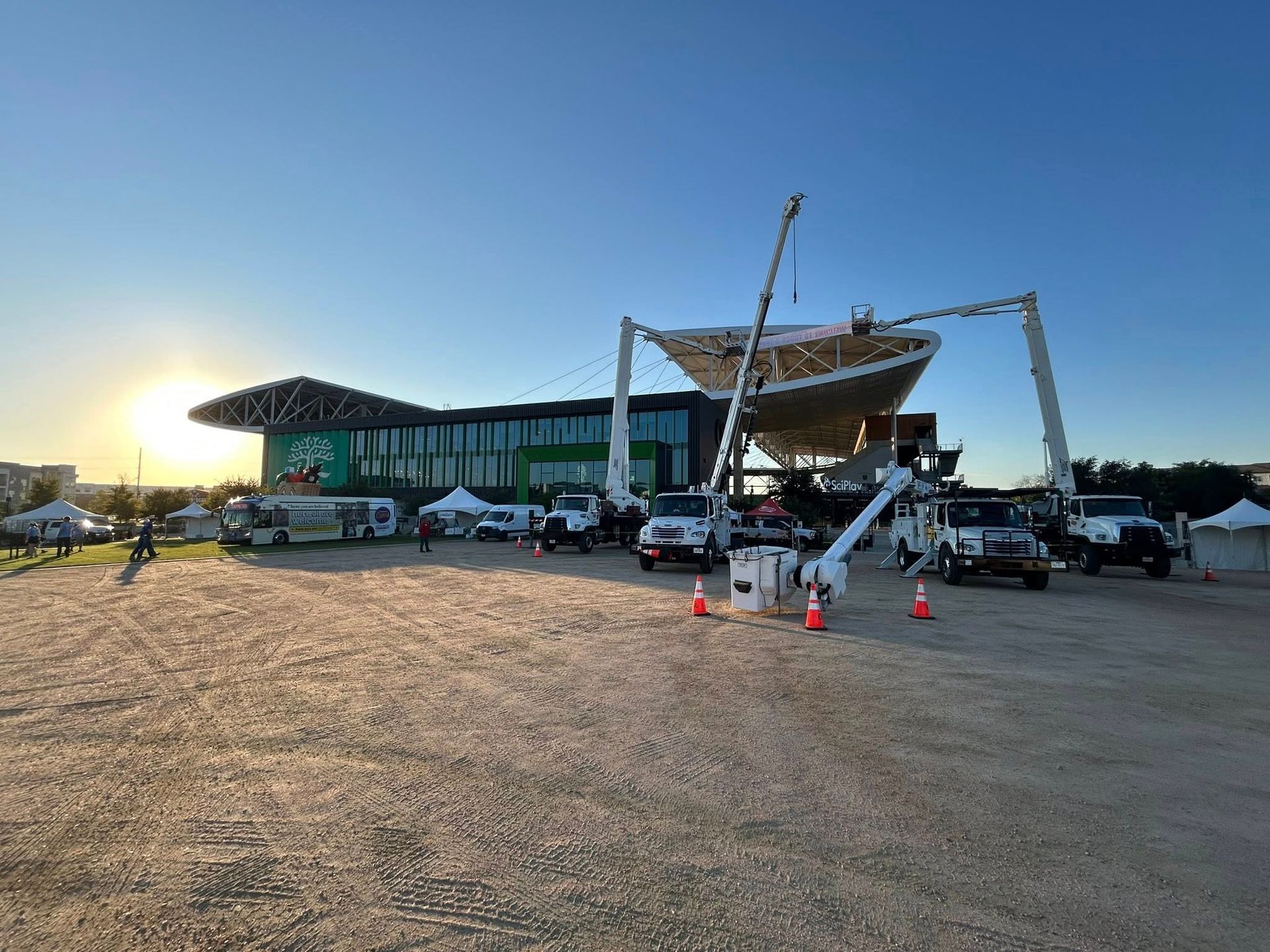 A large sailboat being lifted by cranes outside a modern building at sunset.