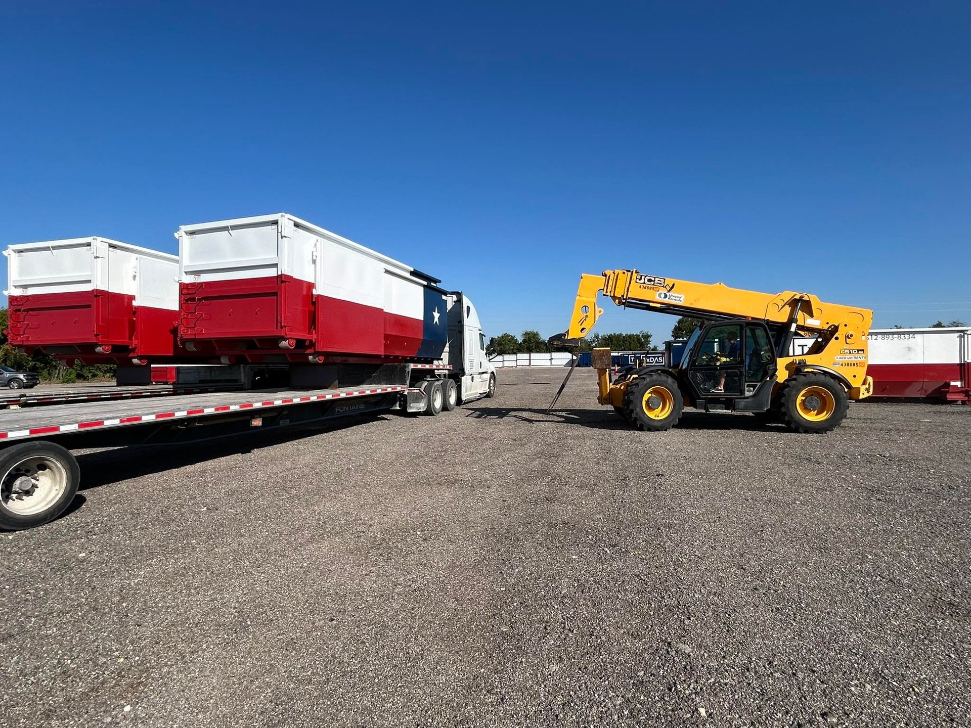 Forklift unloading red and white containers from a flatbed truck on a gravel lot under a blue sky.