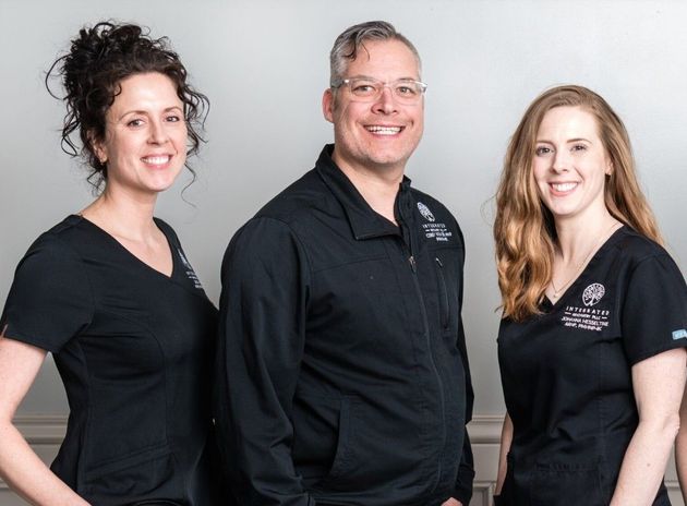 Three people in black shirts standing together and smiling against a light background