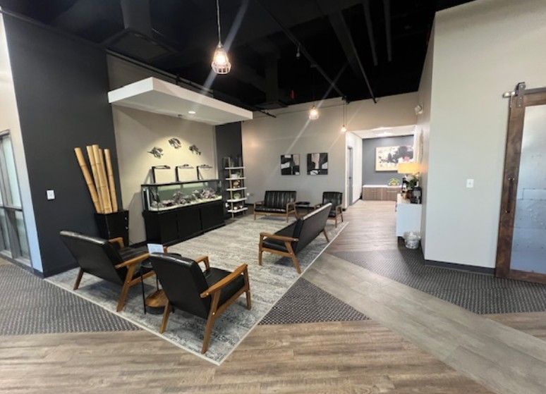 Modern lobby with black chairs, patterned rug, shelves, and a hallway in a gray-and-white interior