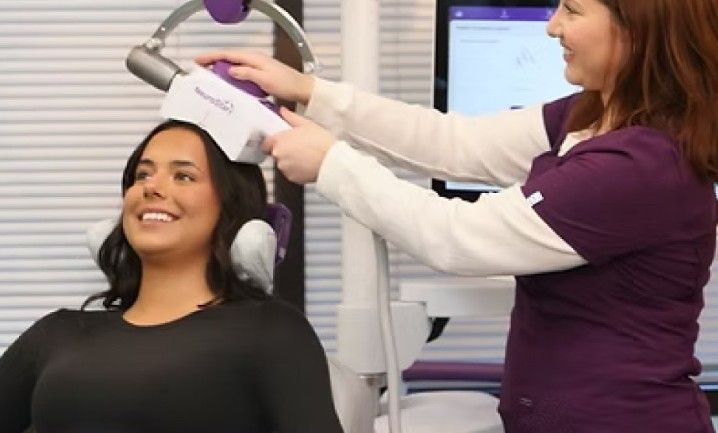 Patient receiving a scalp treatment from a clinician in a medical office, smiling under a white device.