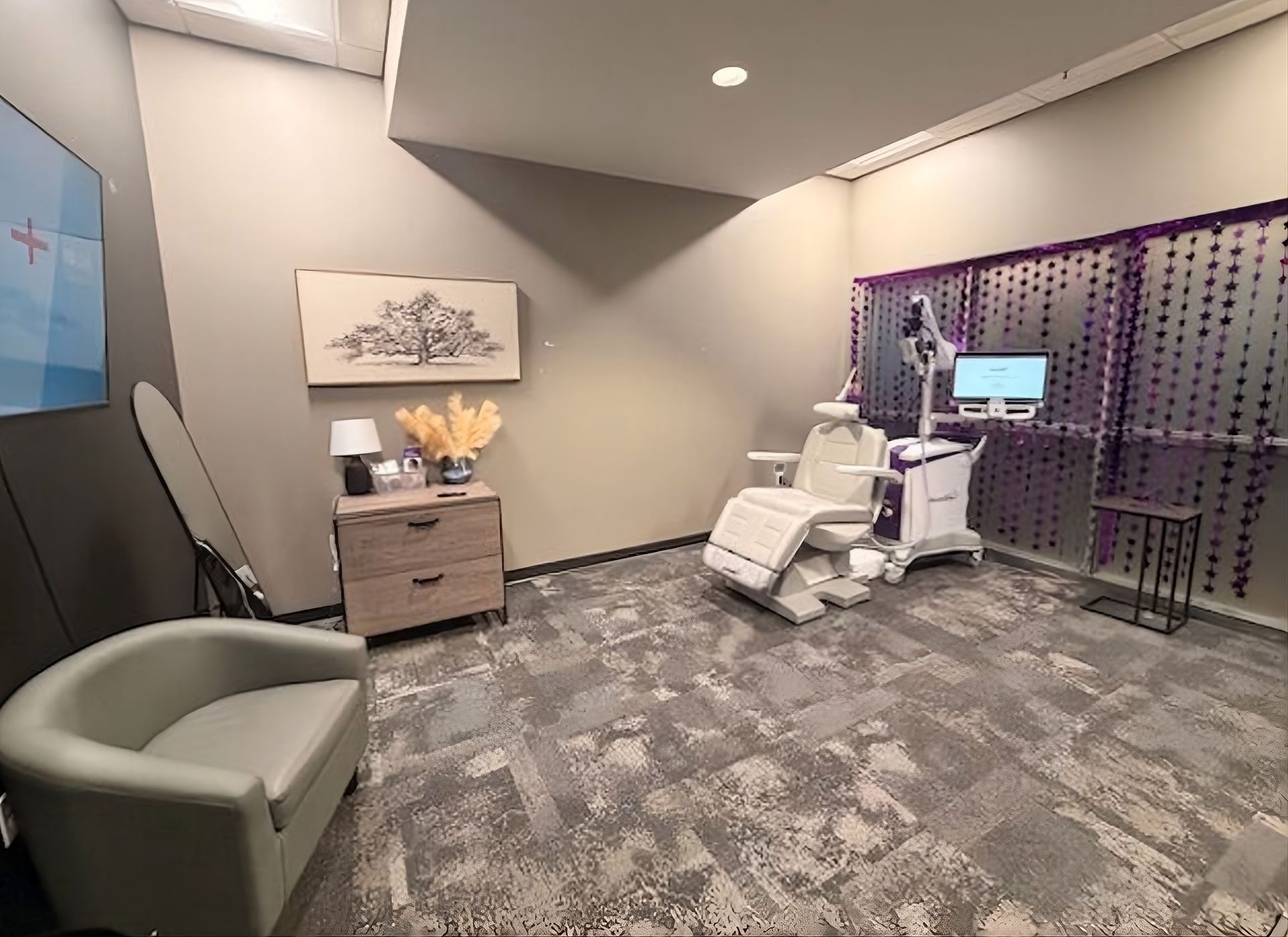 Modern clinic exam room with a recliner, cabinets, patterned wall divider, and medical equipment