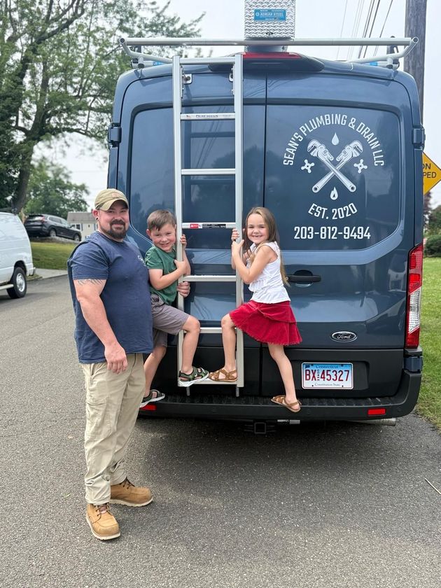 Man standing with two children beside a blue service van with a ladder on the back.