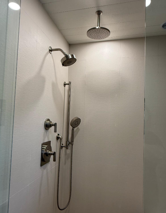 Modern tiled shower with chrome showerhead, handheld sprayer, and wall-mounted controls
