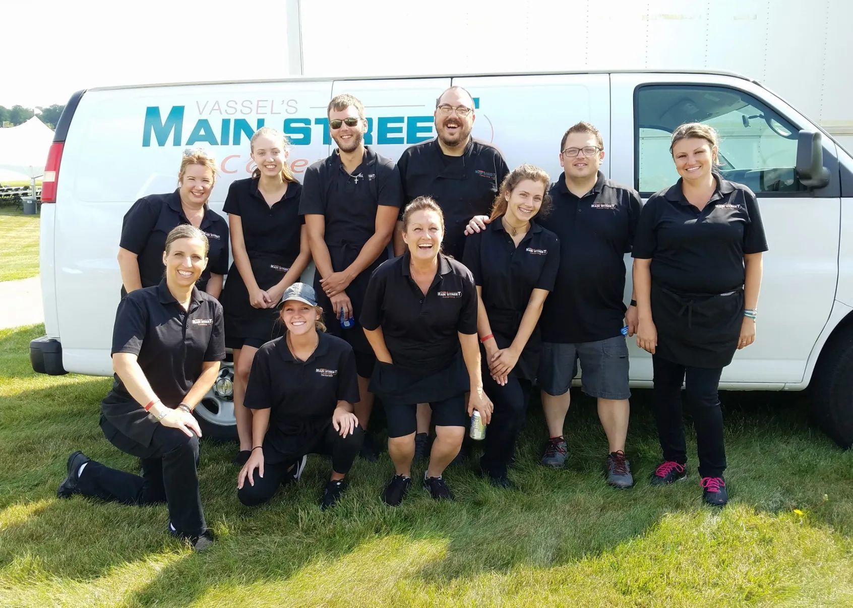 Group of people in black shirts posing by a white van with 