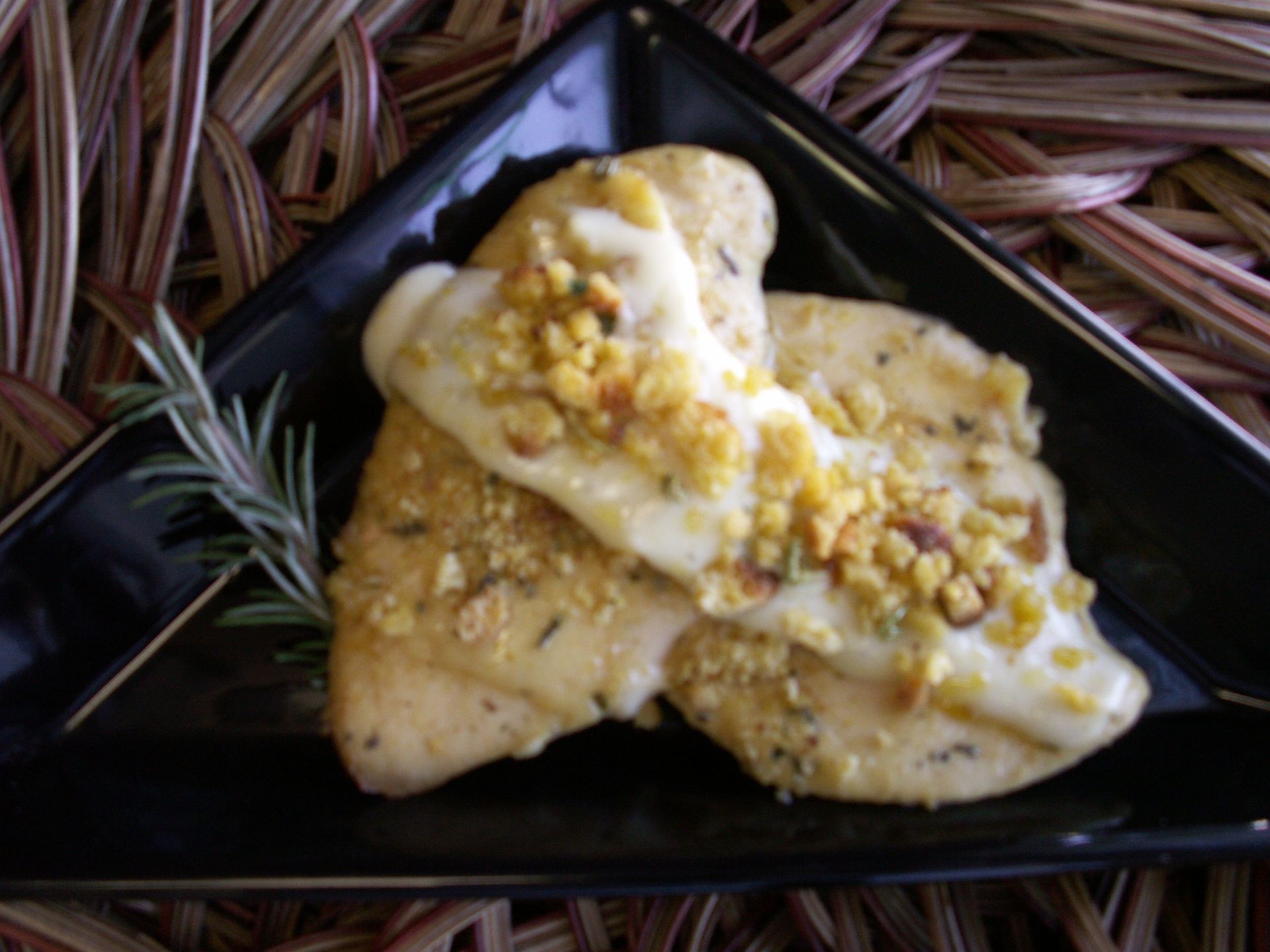Chicken breasts with a crumb topping on a black plate, garnished with rosemary.
