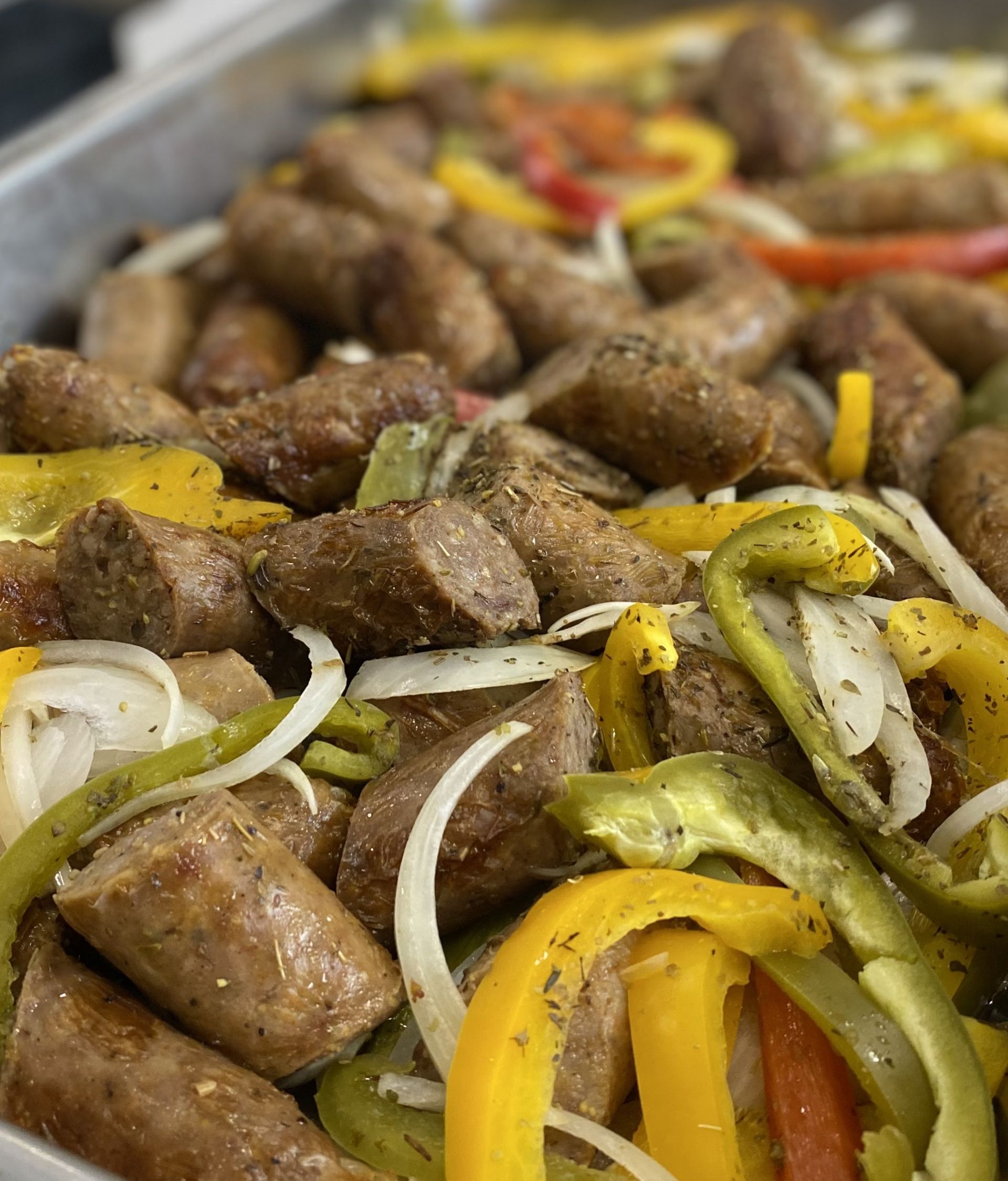 Sausage, sliced peppers, and onions in a tray, seasoned and ready to serve.