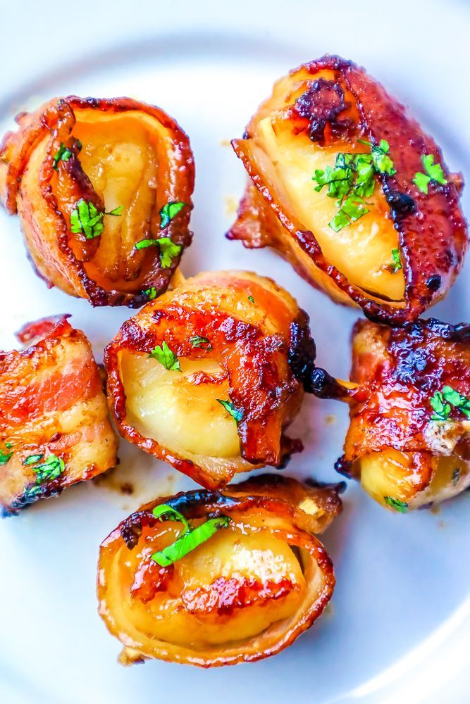 Bacon-wrapped potatoes on a white plate, glistening with a glaze and garnished with green herbs.