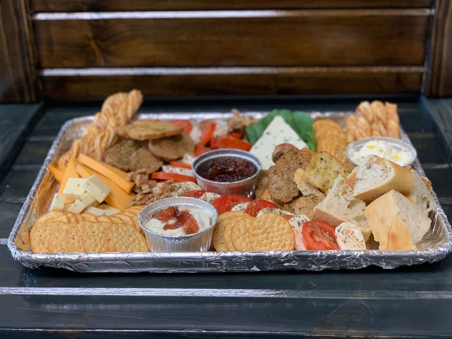 Charcuterie board with cheeses, crackers, bread, and dips on a silver tray, set on a wooden surface.