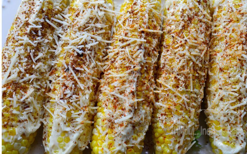 Grilled corn on the cob, slathered in sauce, and sprinkled with cheese and seasoning.