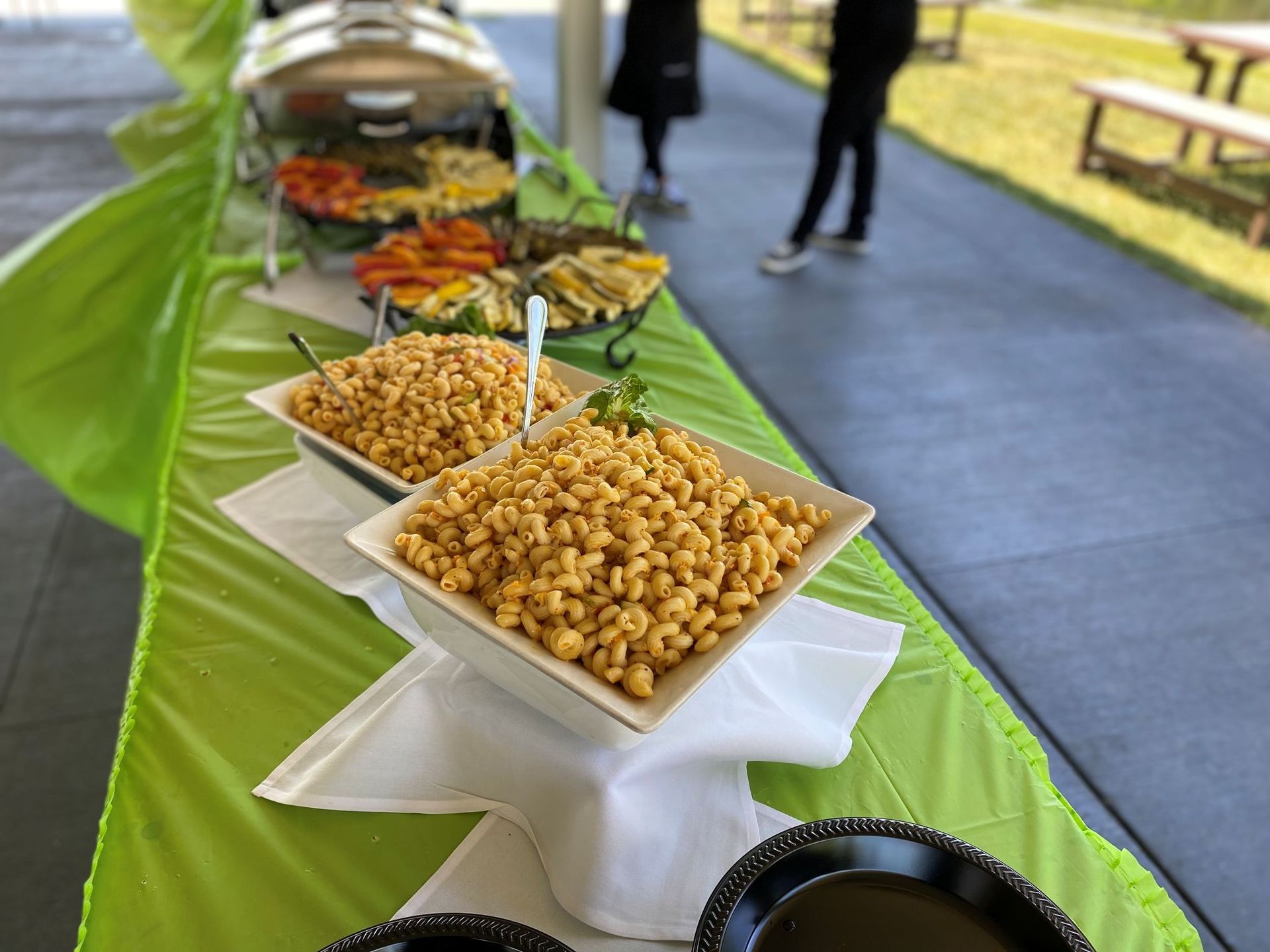 Buffet table with golden pasta, roasted vegetables, and serving staff in the background.