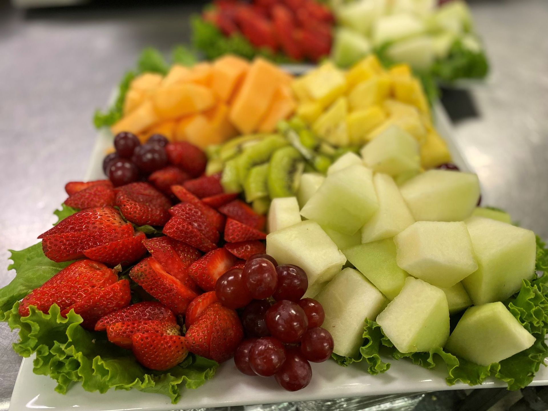 Fruit platter with strawberries, grapes, melon, kiwi, pineapple, and apples arranged on lettuce.