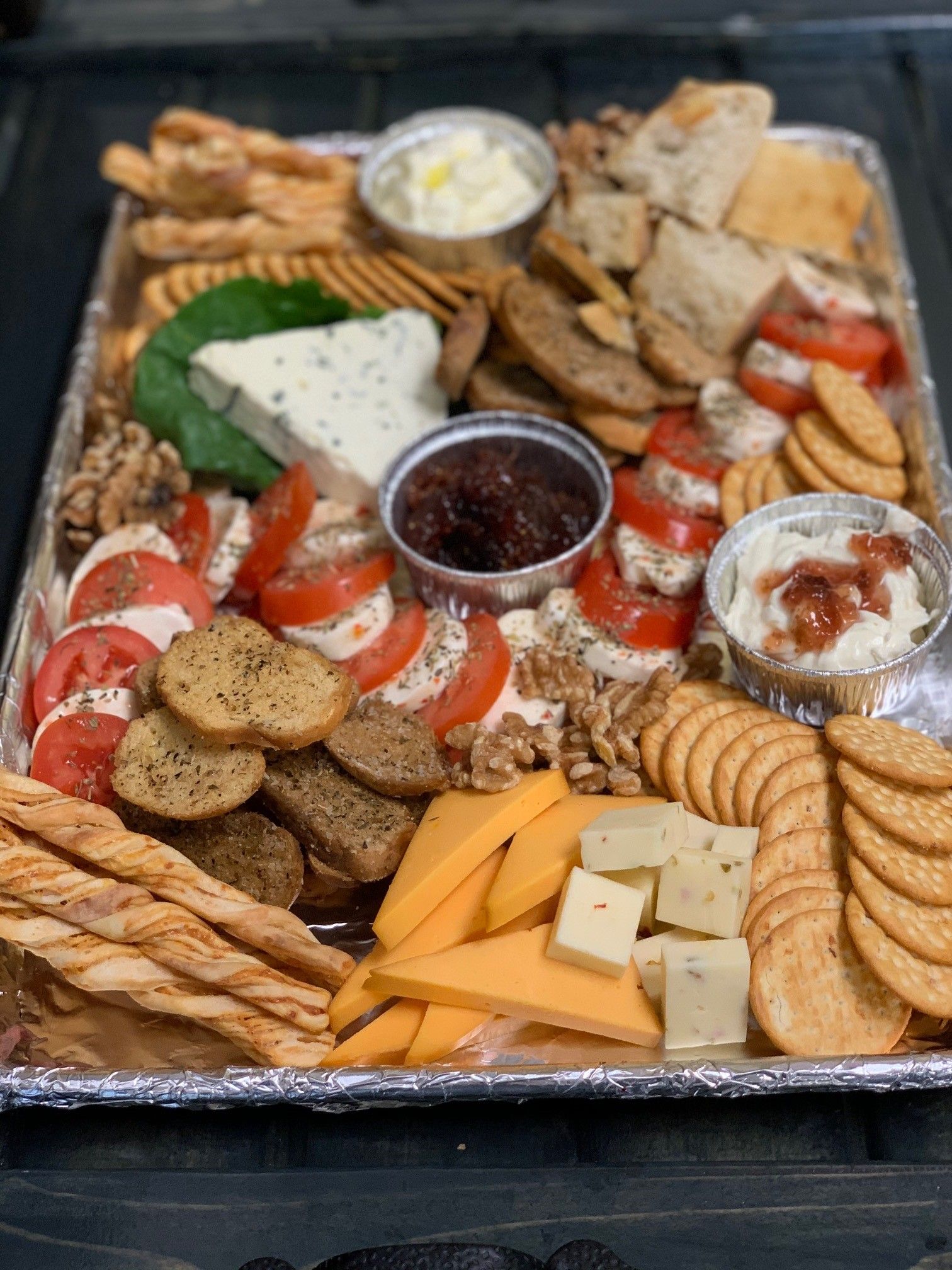 Charcuterie board with cheeses, crackers, tomatoes, dip, and bread.