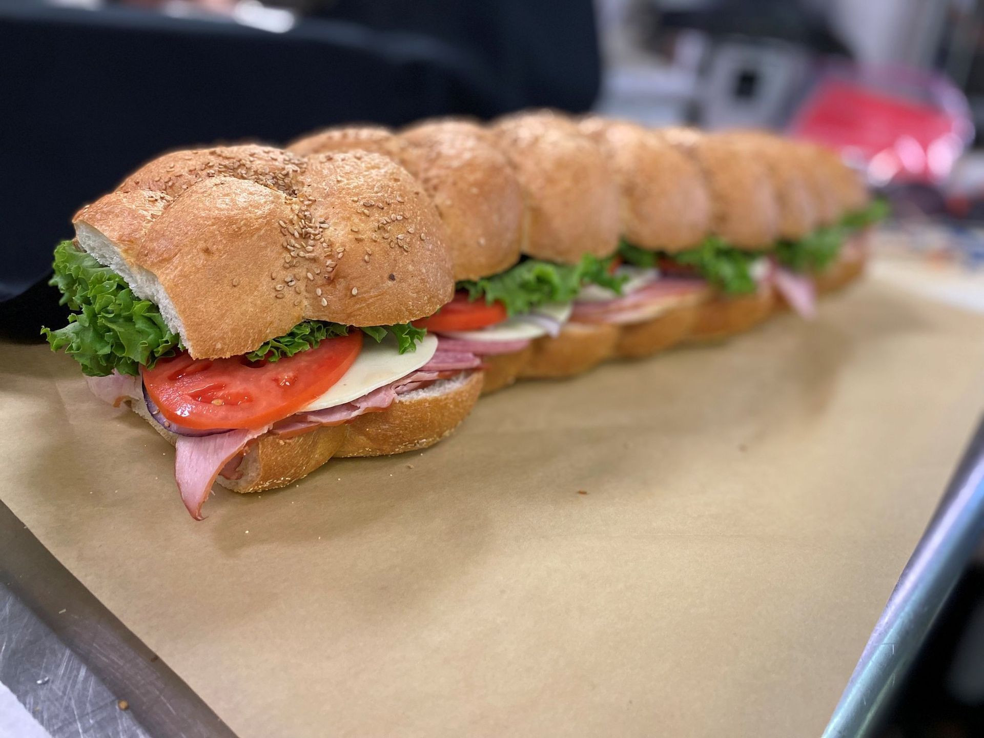 Giant sandwich with multiple sections, containing lettuce, tomato, ham, and cheese on a seeded roll, on a brown surface.