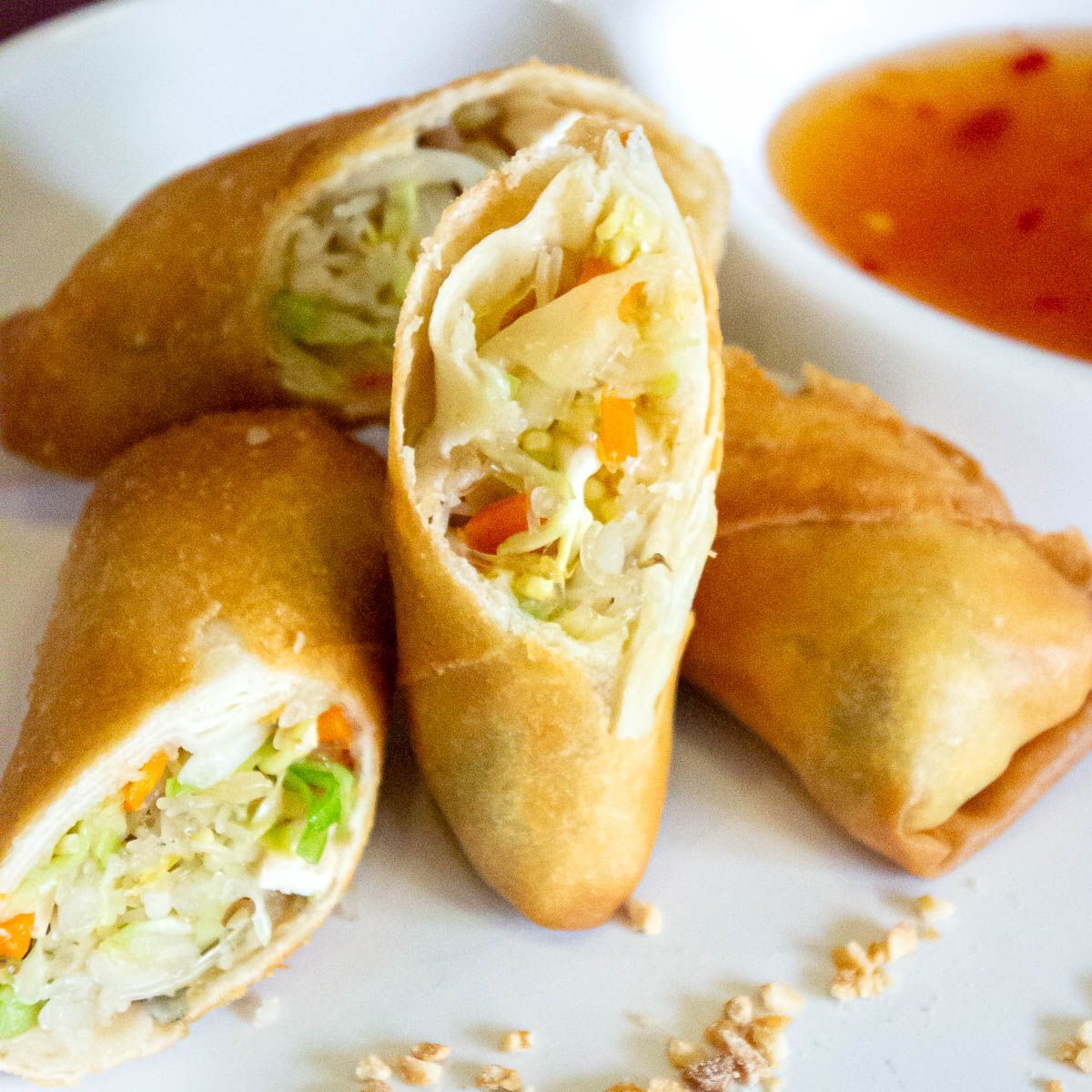 Golden fried spring rolls, cut open to reveal vegetable filling, with dipping sauce.