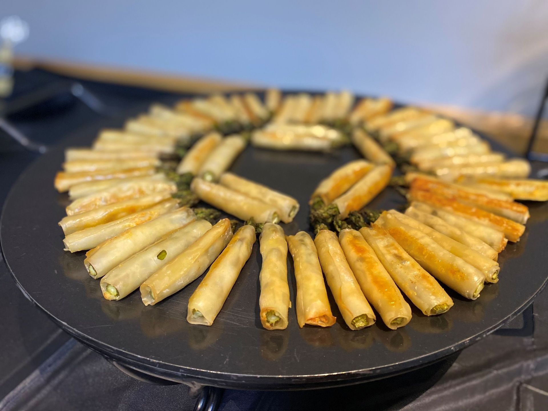 Fried spring rolls arranged in a circle on a dark plate.