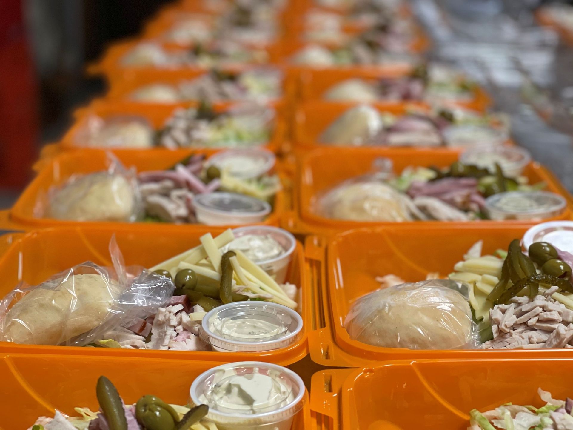 Orange food containers filled with salad, pickles, rolls, and dressing, ready for delivery.