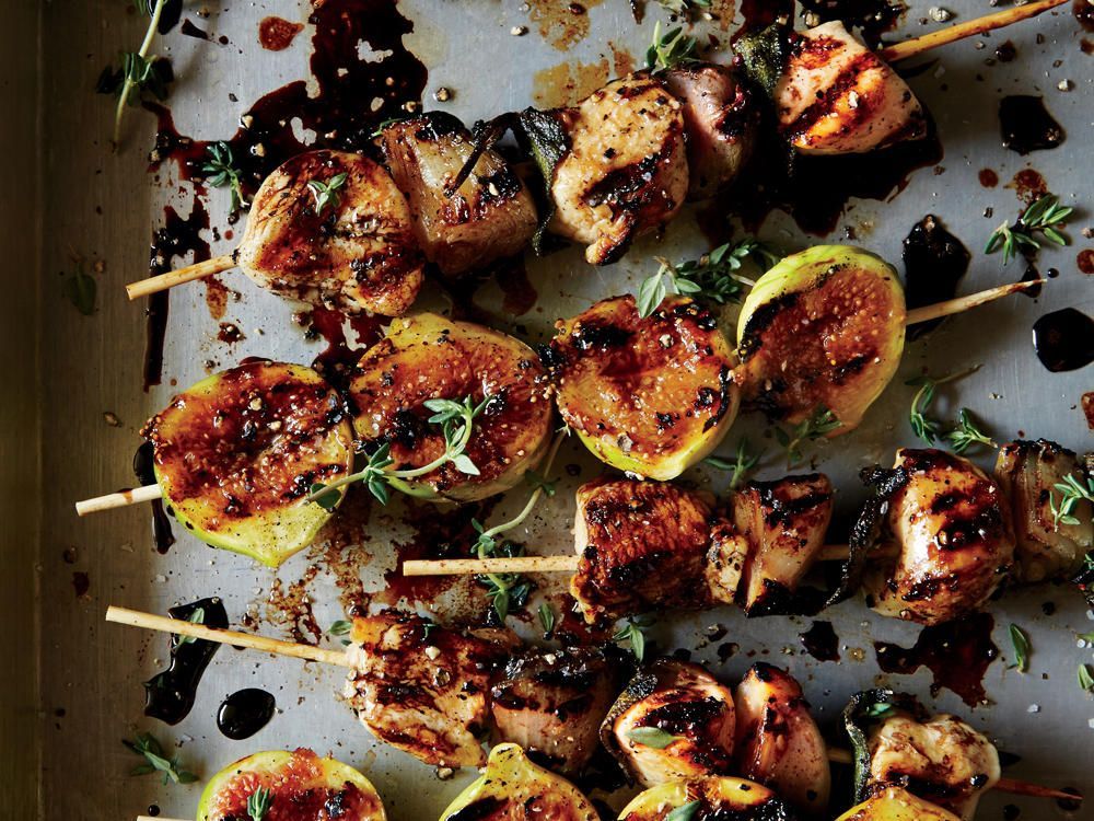 Grilled skewers with fruit and meat, drizzled with glaze and herbs on a baking sheet.