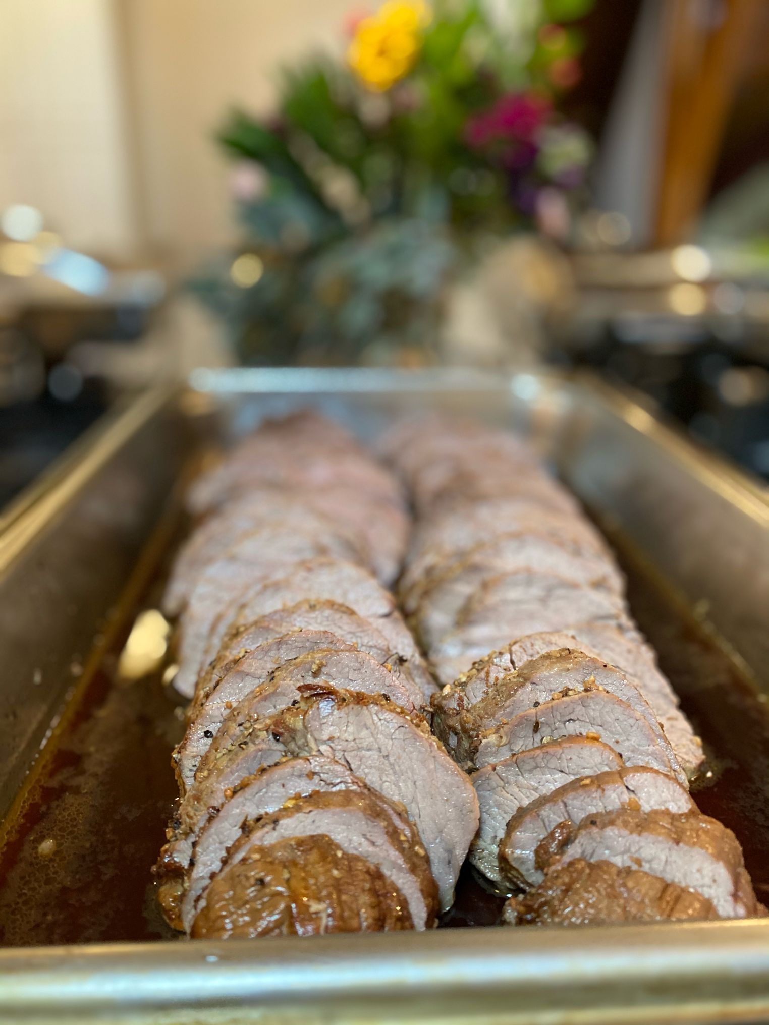 Sliced roast beef in a pan, shallow focus with flowers blurred in the background.