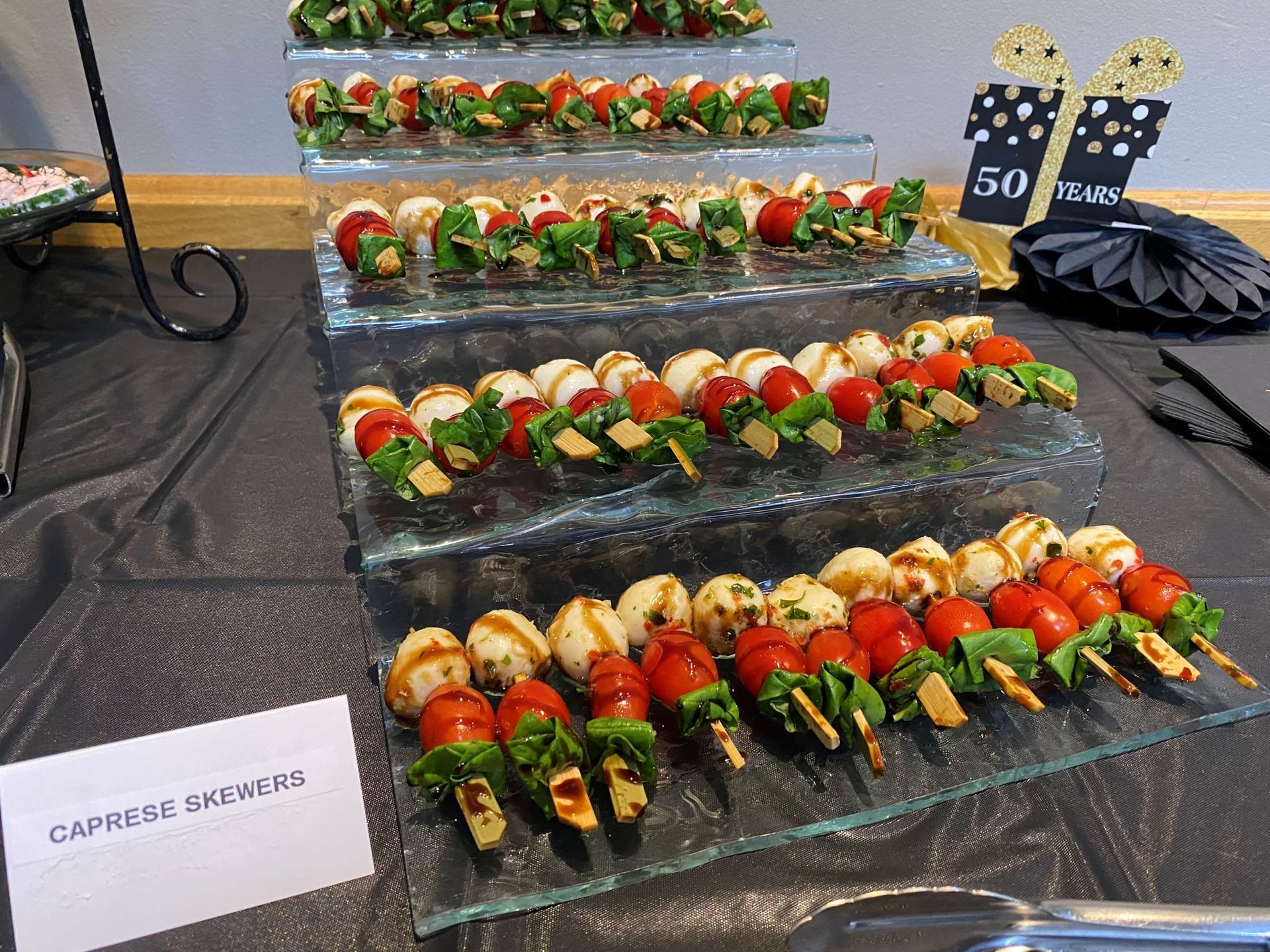 Caprese skewers on a tiered glass display at a party. Red tomatoes, mozzarella, and basil.