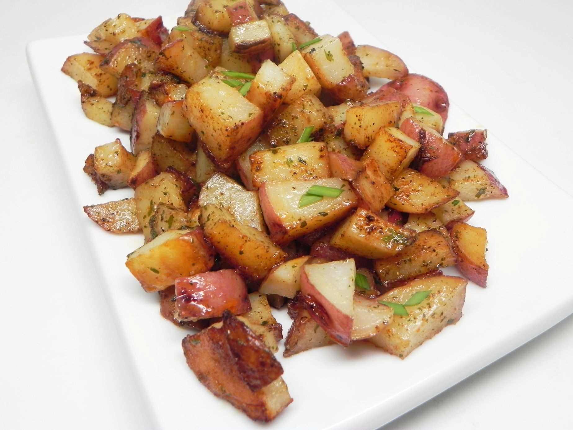 Roasted red potatoes on a white plate, seasoned with herbs and spices.