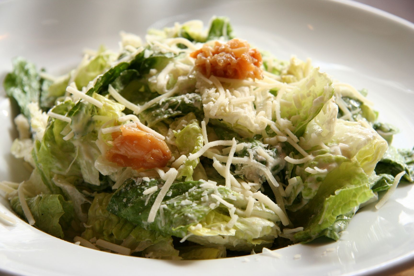 Caesar salad in a white bowl, romaine lettuce, grated cheese, creamy dressing, and croutons.
